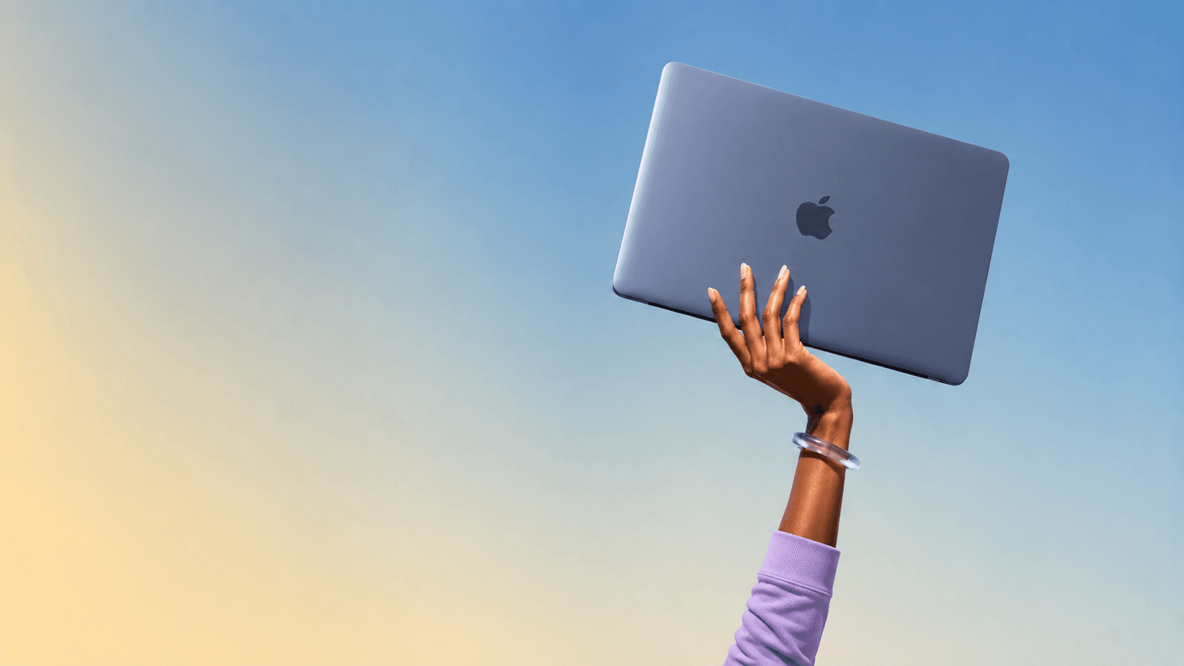 A hand holding a MacBook up against a bright sky