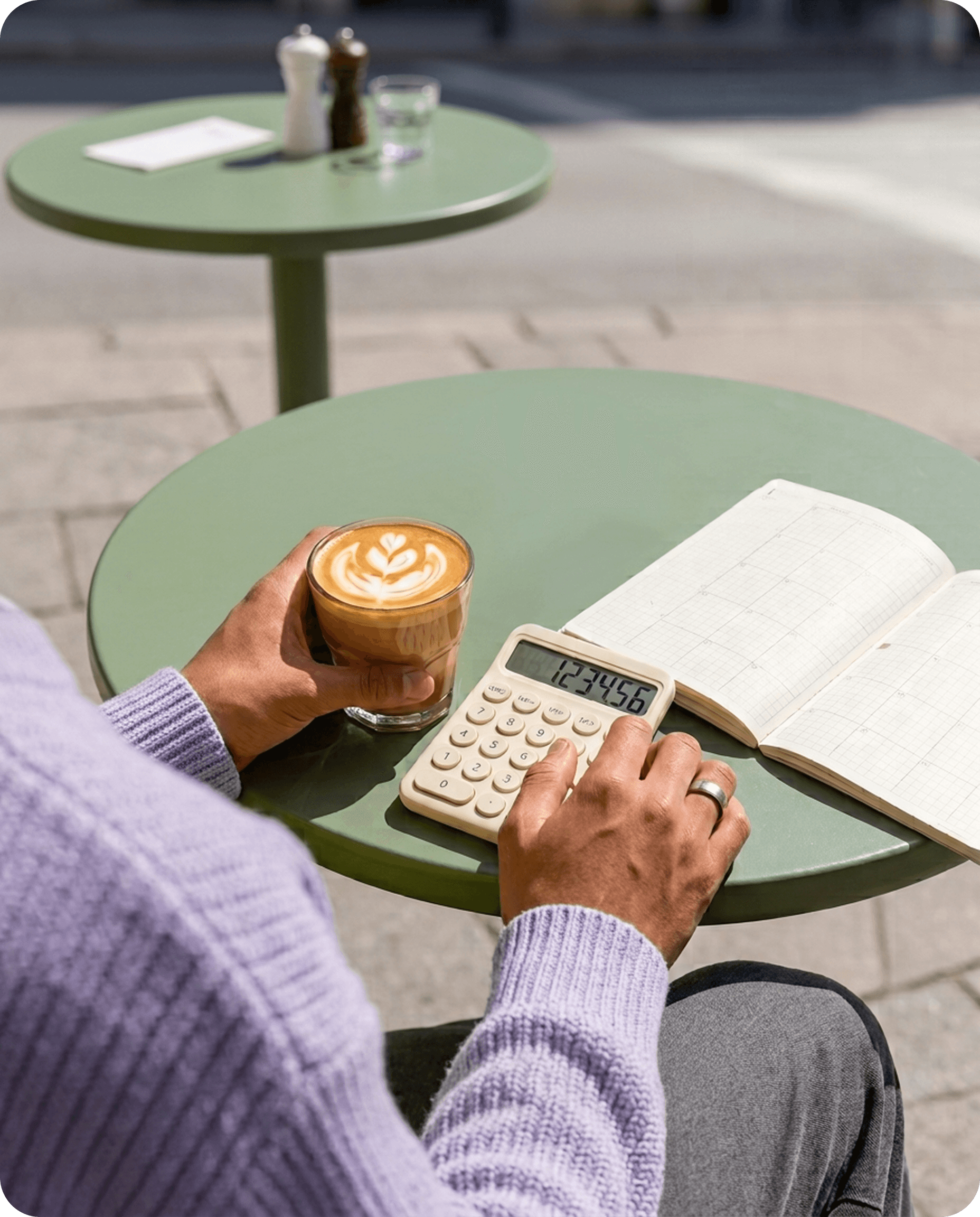A student calculating monthly costs with a calculator and notebook at a cafe table